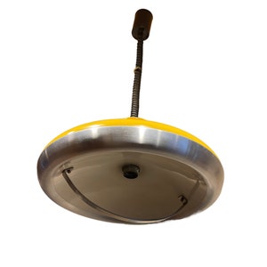 May include: A yellow and silver pendant light with a long, thin cord. The light has a round, saucer-shaped shade with a silver rim.