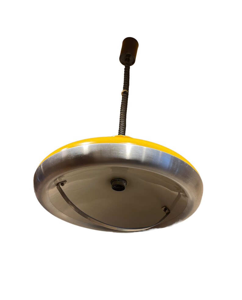 May include: A yellow and silver pendant light with a long, thin cord. The light has a round, saucer-shaped shade with a silver rim.