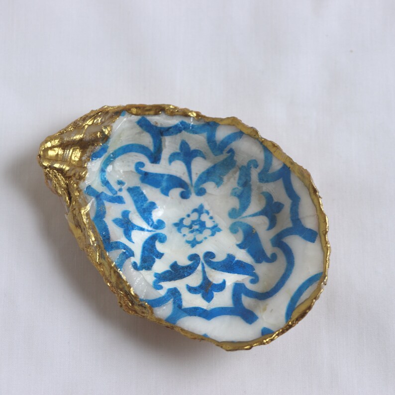 May include: A white oyster shell with a blue and white patterned design and a gold rim.