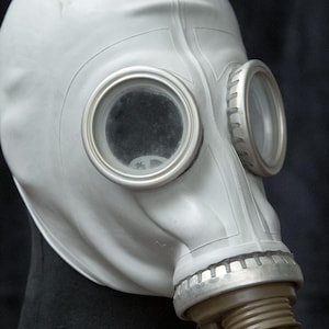 Könnte beinhalten: Eine weiße Gasmaske mit zwei runden Augenöffnungen und einem Metallmundstück. Die Maske steht auf einem schwarzen Ständer.