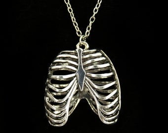 Puede incluir: Collar de plata con un colgante de caja torácica detallada. El colgante es una representación realista de una caja torácica humana.