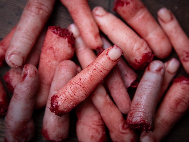 May include: A pile of fake, bloody fingers, some with the tips cut off, arranged on a wooden surface.