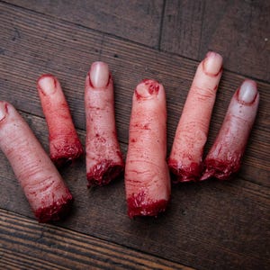 May include: Five severed, bloody fingers on a wooden surface. The fingers are realistic and detailed, with visible blood and flesh.