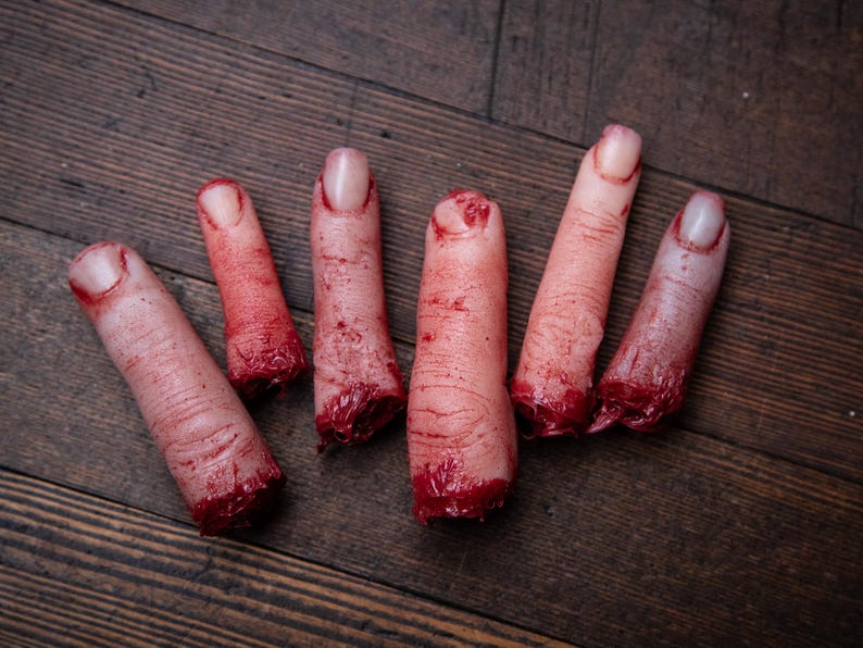 May include: Five severed, bloody fingers on a wooden surface. The fingers are realistic and detailed, with visible blood and flesh.