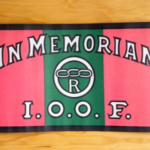 Może przedstawiać: Czerwono-zielona flaga z napisem "IN MEMORIAM" i "I.O.O.F." białymi literami. W środku flagi znajduje się białe koło z łańcuchem i literą "R".