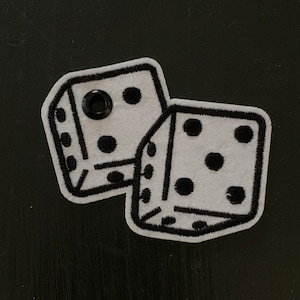May include: Two white dice patches with black outlines and black dots. One patch has a black grommet. The dice show the numbers 1, 2, 3, 4, 5, and 6. The patches are on a black surface.
