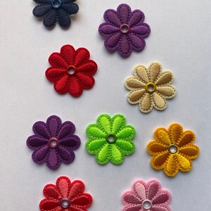 May include: Assortment of ten embroidered fabric flower shapes with a buttonhole in the center. The flowers are in various colors including red, pink, purple, green, yellow, orange, and blue.