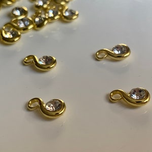 May include: Four gold-toned metal charms with clear rhinestone accents. Each charm is shaped like a sideways 'S' with a round rhinestone in the center.