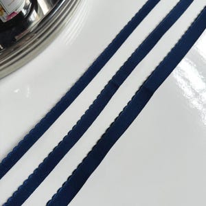 May include: Three navy blue elastic ribbons with a scalloped edge. The ribbons are lying flat on a white surface.