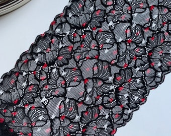 Könnte beinhalten: Schwarze Spitzenborte mit floralem Muster, versehen mit roten und weißen Akzenten. Die Borte hat einen gewellten Rand und wird auf einer weißen Oberfläche gezeigt. Diese dekorative Borte eignet sich für verschiedene Bastelprojekte.