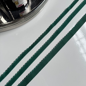 May include: Two pieces of dark green satin ribbon with a scalloped edge. The ribbon is lying on a white surface.