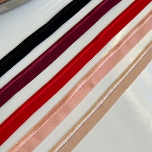 May include: Assortment of narrow, bias-cut fabric strips in various colors. The colors include black, burgundy, red, light pink, and tan. Each strip has a finished edge, and the light pink and tan strips have a decorative stitch.