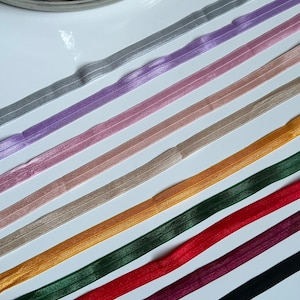 May include: Assortment of 10 colors of elastic ribbon, including gray, purple, pink, beige, gold, green, red, burgundy, and black. The ribbon is flat and has a subtle shimmer.