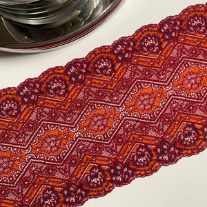 May include: Red and orange lace trim with a geometric pattern. The lace has a scalloped edge.