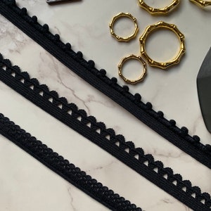 May include: Three black elastic trims with different edging details. The top trim has a pom-pom edging, the middle trim has a scalloped edging, and the bottom trim has a small, rounded edging.