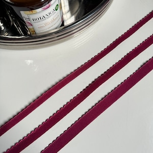 May include: Three pieces of burgundy satin ribbon with scalloped edges. The ribbon is laying on a white surface.