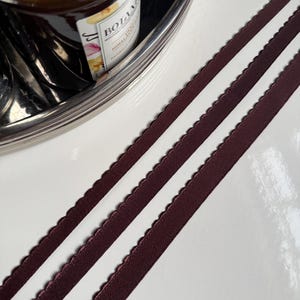 May include: Two brown elastic bands with scalloped edges. The bands are lying on a white surface.