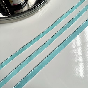 May include: Three strands of light blue satin ribbon with a scalloped edge.