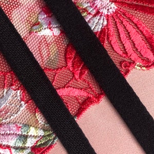 May include: Two black elastic straps against a background of red and white floral lace.