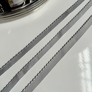 May include: Three silver satin ribbons with scalloped edges. The ribbons are arranged in a diagonal pattern on a white surface.