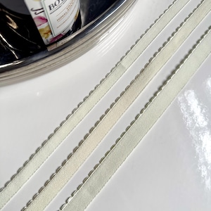 May include: Three pieces of white satin ribbon with a scalloped edge. The ribbon is laying flat on a white surface.