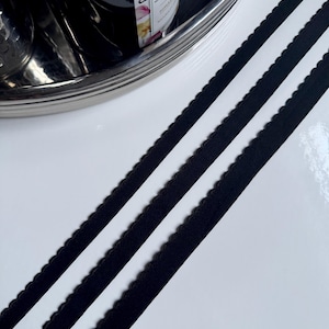May include: Two black elastic bands with a scalloped edge. The bands are lying on a white surface.