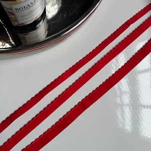 May include: Two red elastic bands with scalloped edges. The bands are lying on a white surface.