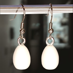 May include: A pair of silver dangle earrings with white oval-shaped beads.