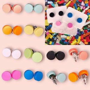 May include: Assortment of colorful round stud earrings. The earrings are made of various materials, including wood, plastic, and metal. The earrings are displayed on a white background.