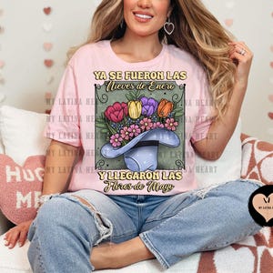 May include: A pink t-shirt with a graphic of a hat with flowers and the text "Ya se fueron las nieves de enero y llegaron las flores de mayo".