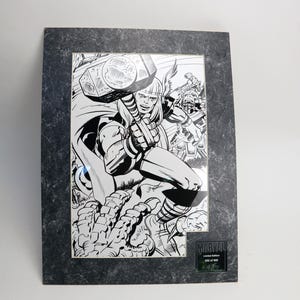 May include: Black and white comic art print of a superhero wielding a hammer, framed in a dark gray textured frame. The print is a limited edition Marvel collectible, numbered 202 of 500.