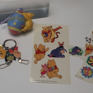 May include: A collection of Winnie the Pooh themed items. Includes a keychain with character charms, stickers, and an Easter egg ornament with "Happy Easter" text. The stickers feature Pooh, Piglet, Tigger, and Eeyore.