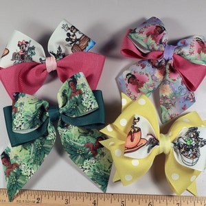May include: Six colorful hair bows with various designs. One bow features a yellow polka dot pattern with a teacup graphic. Other bows have cartoon character prints and solid colors like pink and teal.