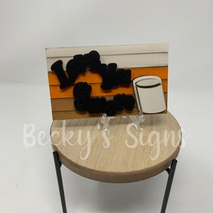 May include: A wooden sign with the text "Love You More" in black letters on a white and orange striped background. A white mug with a black outline is on the right side of the sign.