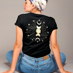 May include: A black t-shirt with a gold moon and stars design on the back. The design features a crescent moon, a full moon, and a crescent moon with a star inside. The design is surrounded by a circle of stars.