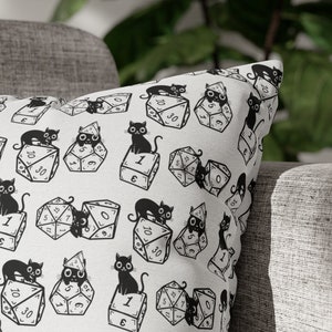 May include: White throw pillow with a black and white pattern of cats sitting on dice. The dice have numbers from 1 to 20.