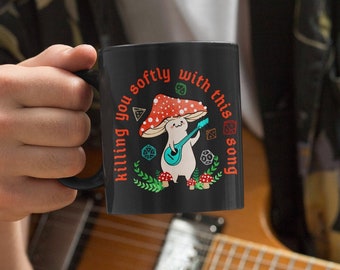 May include: Black coffee mug with a white design of a mushroom character playing a guitar with the text "Killing you softly with this song".