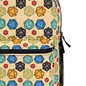 May include: A beige backpack with a repeating pattern of colourful twenty-sided dice. The dice are in various colours, including red, yellow, blue, green, and black.