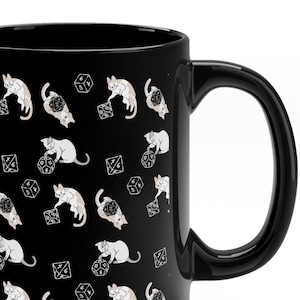 May include: Black ceramic coffee mug with a white cat and dice pattern. The mug has a black handle.
