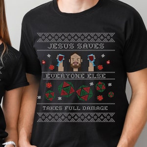 May include: Two black t-shirts with a Christmas sweater design featuring a cartoon man holding two glasses of wine. The text on the shirts reads "Jesus Saves Everyone Else Takes Full Damage".