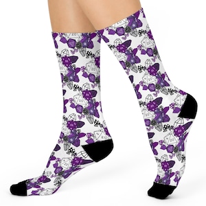 May include: White socks with a repeating pattern of purple, gray, and white dice, crystals, and mushrooms. The socks have black heels and toes. The dice show the number 20.