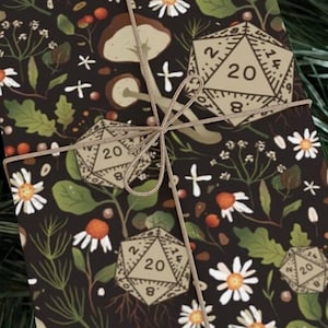 May include: Gift-wrapped package with a dark background featuring a botanical pattern of daisies, leaves, mushrooms, and D20 dice. The package is tied with twine, creating a rustic and whimsical aesthetic.