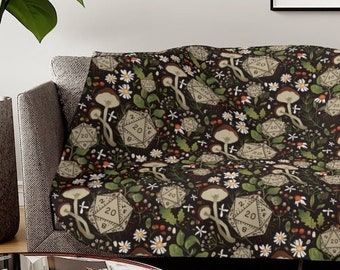 May include: A black and green throw blanket with a repeating pattern of dice, mushrooms, and flowers. The dice are 20-sided and have the number 20 printed on them.