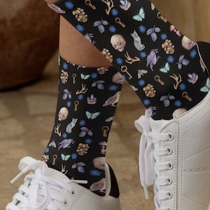 May include: A pair of black socks with a colorful pattern of keys, butterflies, skulls, and other whimsical designs. The socks are worn with white sneakers.