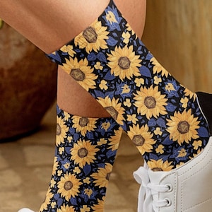 May include: A pair of white sneakers with black trim and sunflower socks. The socks have a blue background with yellow sunflowers.