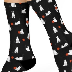 May include: A pair of black socks with a white ghost cat pattern. The cats are holding orange yarn balls.