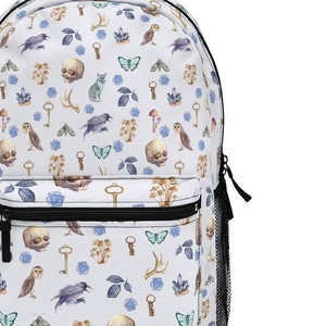 May include: White canvas backpack with a repeating pattern of watercolour illustrations. The pattern includes skulls, owls, butterflies, keys, crystals, and leaves. The backpack has a black zipper and a black mesh pocket on the side.