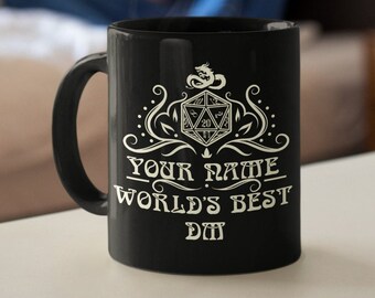 May include: Black ceramic mug with a white graphic design featuring a dragon, a 20-sided die, and the text "YOUR NAME WORLD'S BEST DM". The mug has a curved handle and is sitting on a white surface.