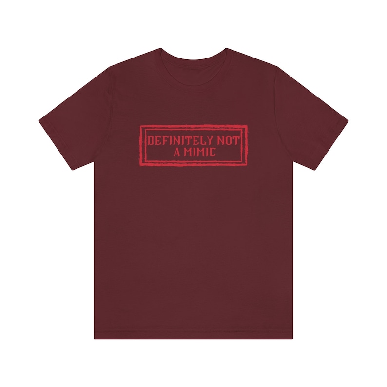 May include: Burgundy t-shirt with a red graphic that says "DEFINITELY NOT A MIMIC" in a vintage-style stamp.