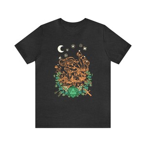 May include: A dark heather grey t-shirt with a graphic of mushrooms, a crescent moon, stars, and a green 20-sided die. The graphic is surrounded by green foliage and a sword.